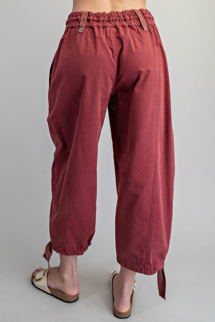 A person shown from the back wearing loose, wide-leg cropped pants in a muted burgundy or dusty rose tone, paired with beige slide sandals, against a plain light gray studio background.