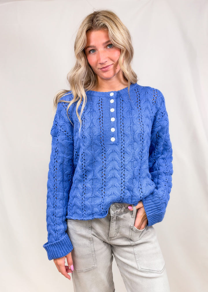 Woman wearing blue cable knit henley pullover on plain background