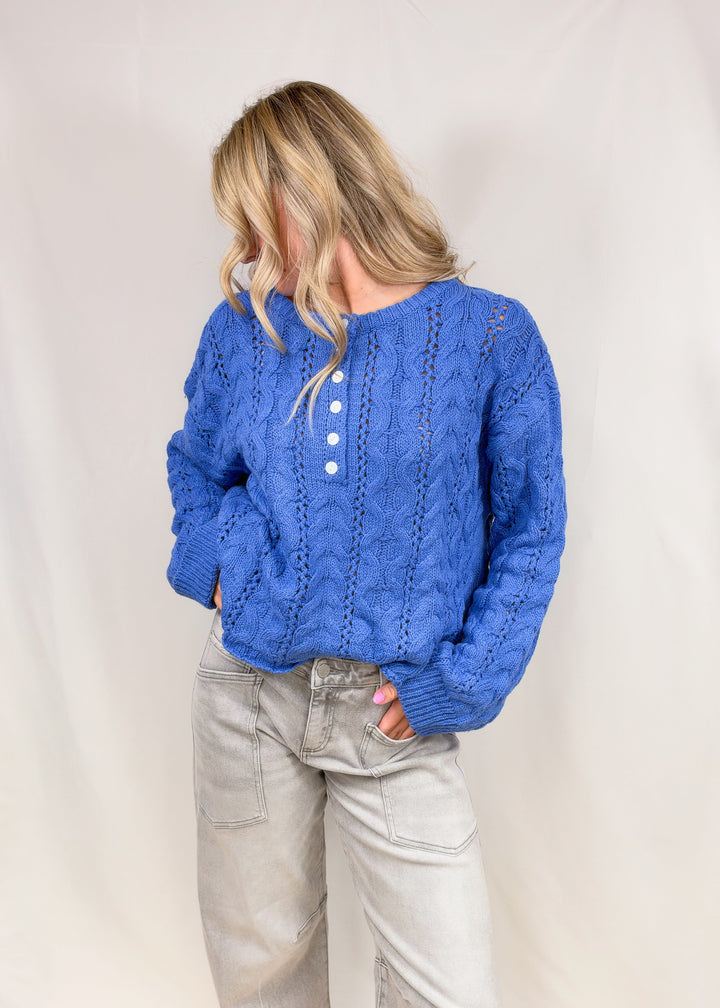 Woman wearing blue cable knit henley pullover on plain background