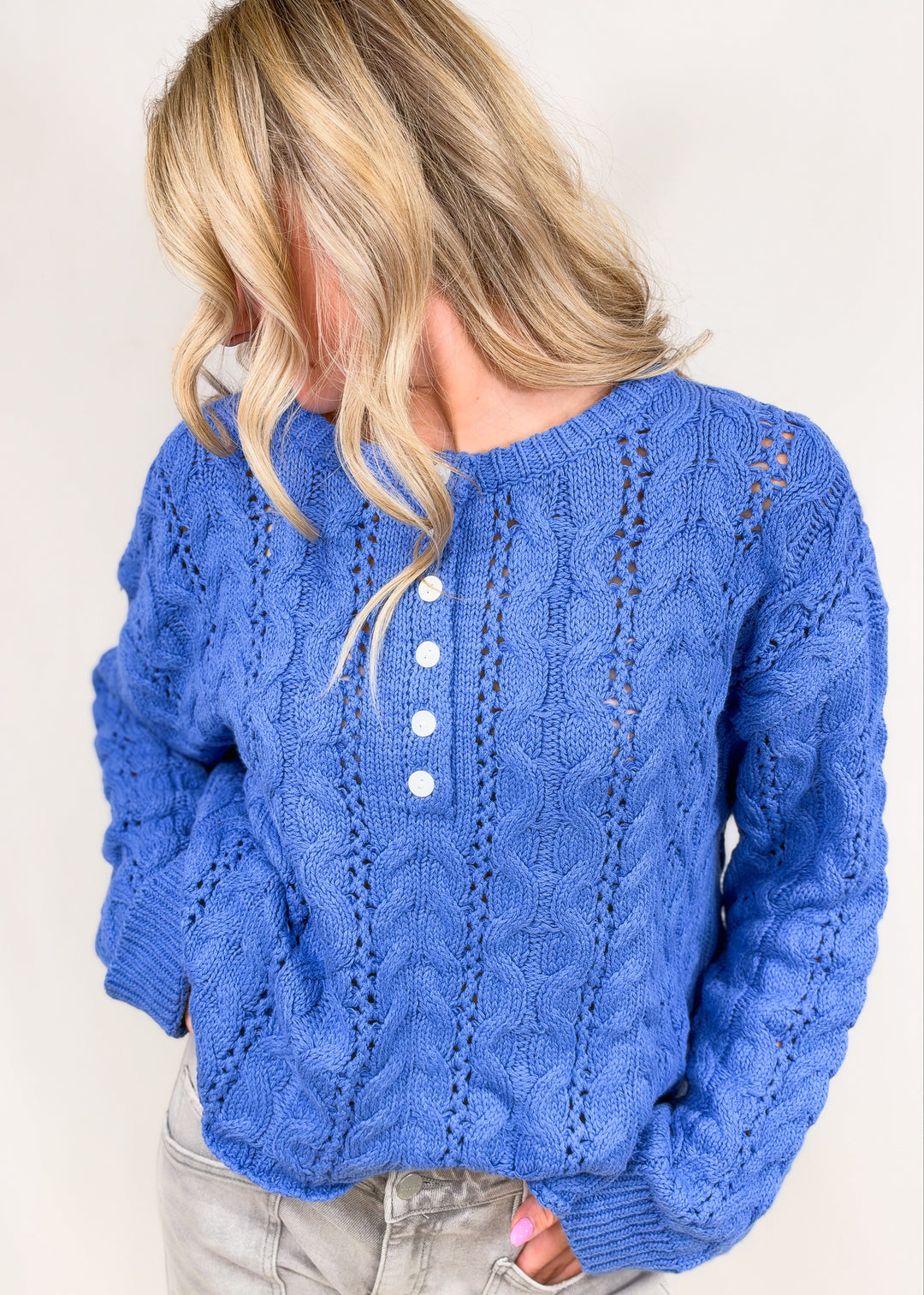 Woman shown from side view wearing blue cable knit henley pullover on plain background