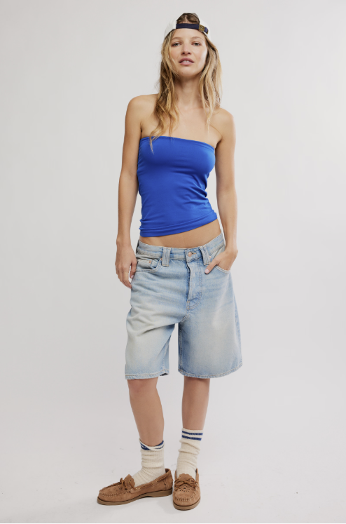 Woman wearing a blue strapless top and denim shorts on a plain background