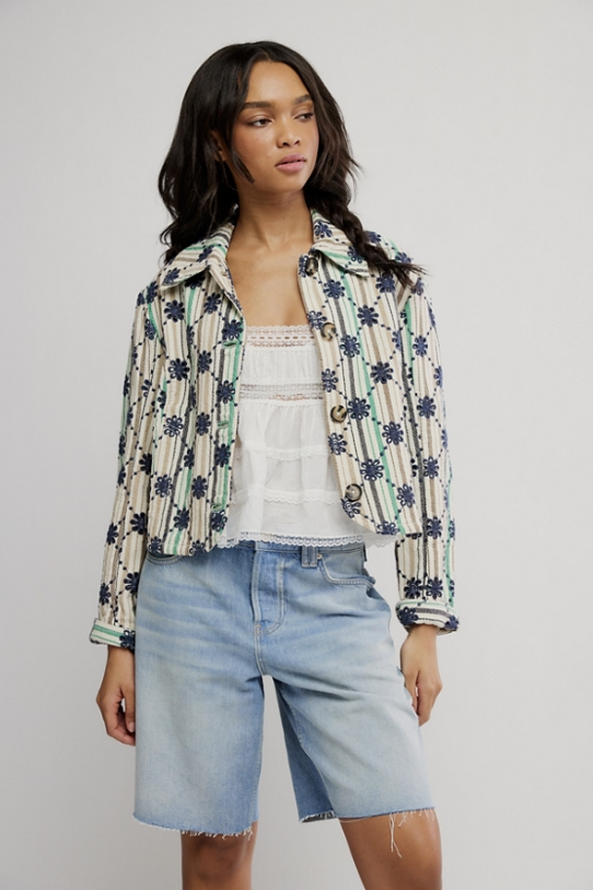 Woman wearing a patterned jacket and denim shorts on a plain background