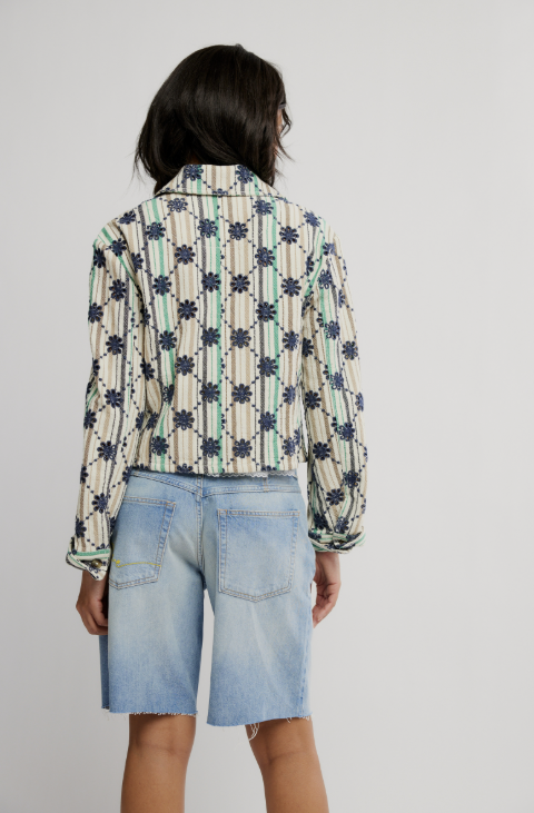 Person wearing a patterned shirt and denim shorts on a plain background