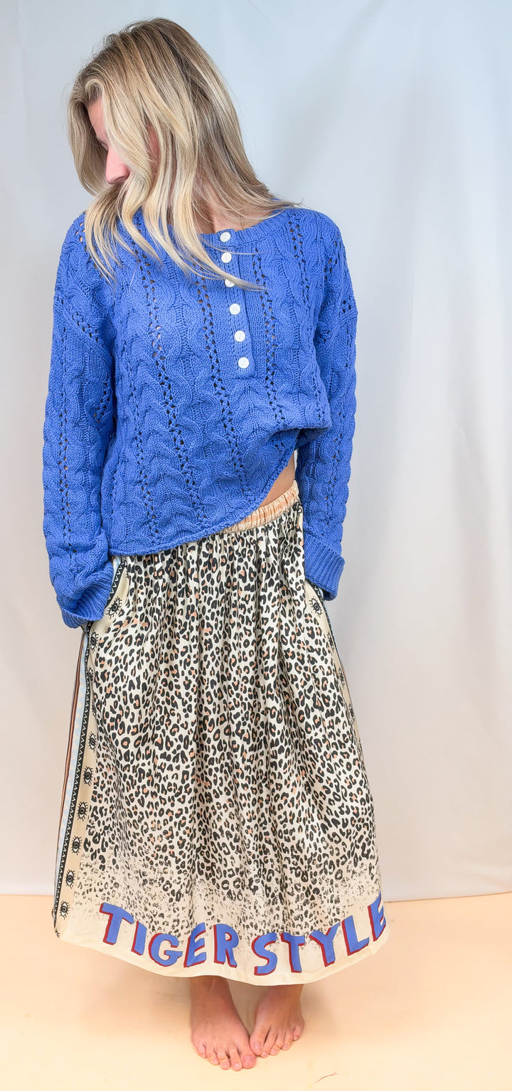 Woman wearing blue sweater and leopard print satin skirt on plain background