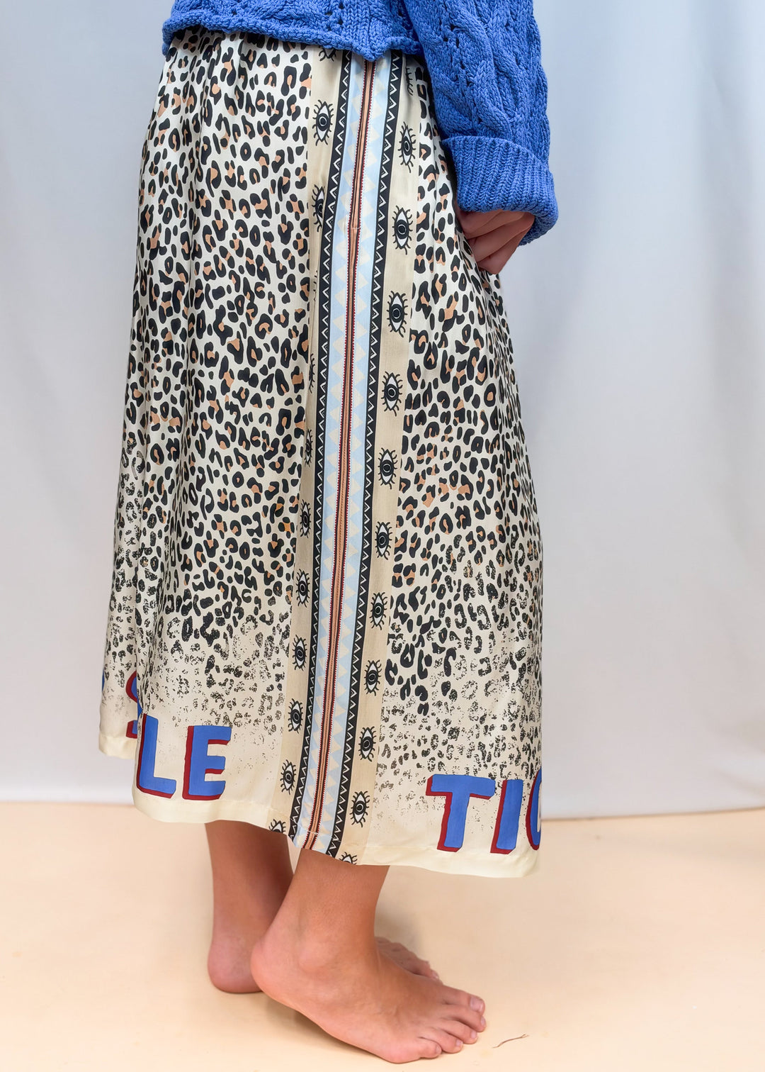 Woman shown from waist down side view wearing leopard skirt on plain background