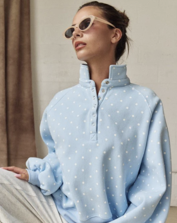 Woman wearing light blue polka dot pullover on plain background