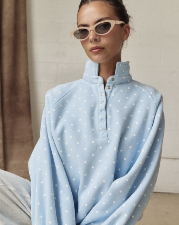 Woman wearing light blue polka dot pullover on plain background