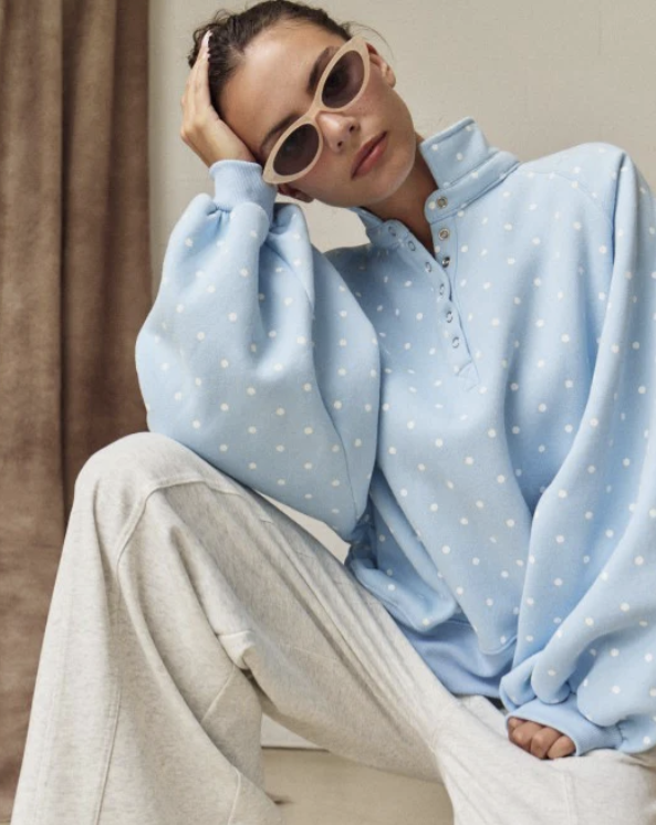 Woman wearing light blue polka dot pullover on plain background