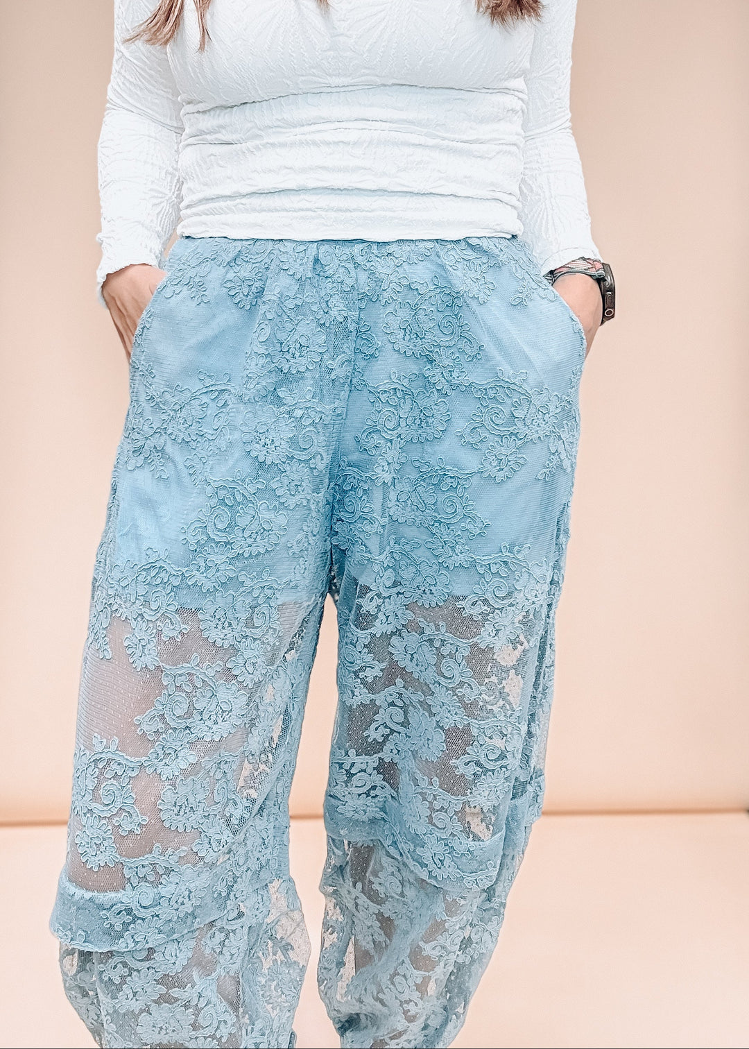 Woman wearing blue lace pants with white shirt on plain background
