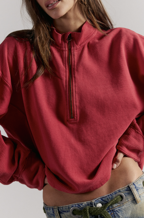 Woman wearing red quarter zip top and blue jeans on white background