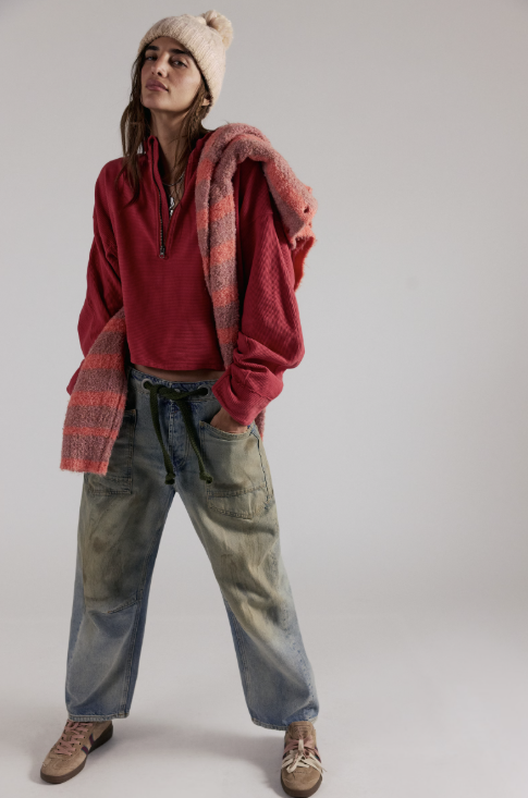 Woman wearing red quarter zip and blue jeans on white background