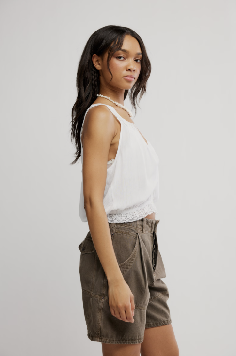 Woman wearing a white tank top and brown shorts on a plain background
