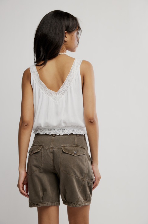 Back of woman wearing white tank and brown shorts on white background
