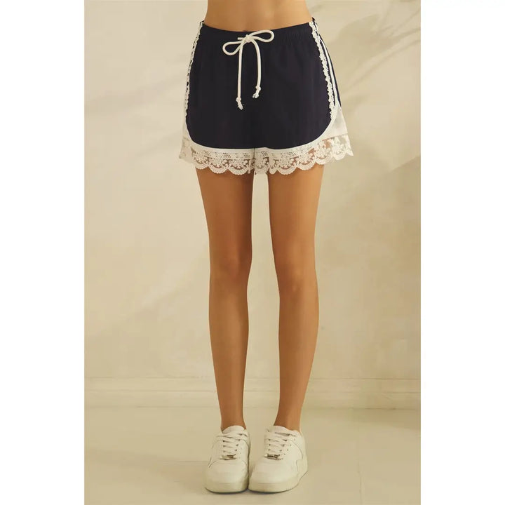 Woman wearing navy satin shorts with lace trim on plain background