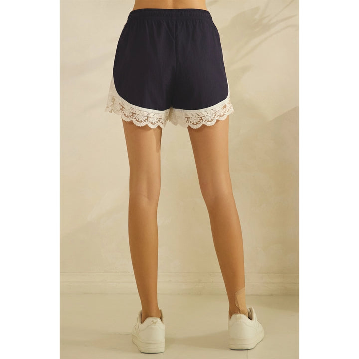 Person wearing navy shorts with white lace trim on a neutral background