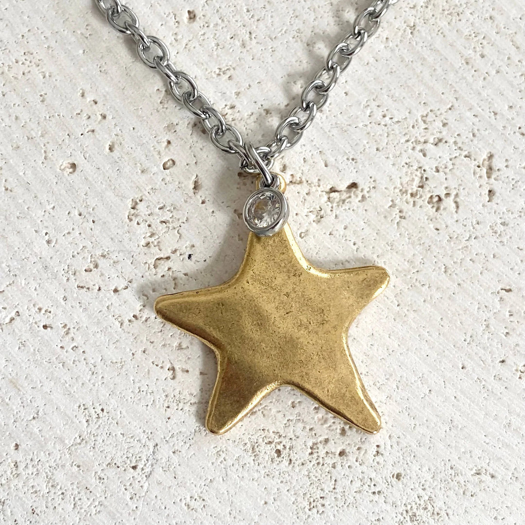 gold star necklace on silver chain on plain background