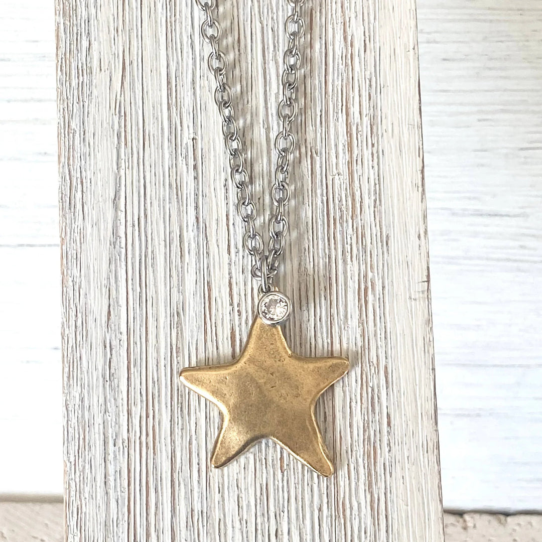 Gold star pendant necklace on a chain against a light wooden background