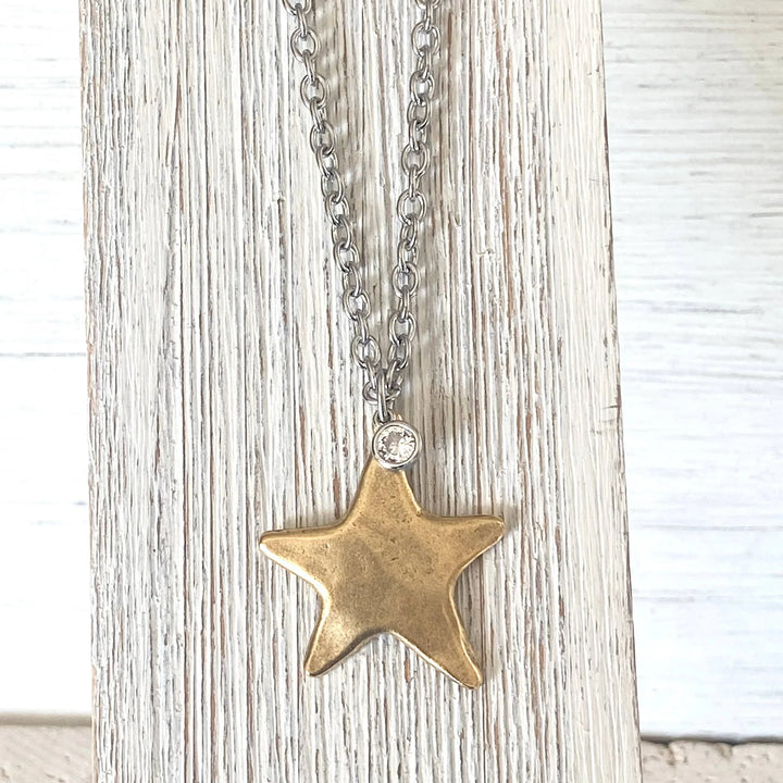 Gold star pendant necklace on a chain against a light wooden background