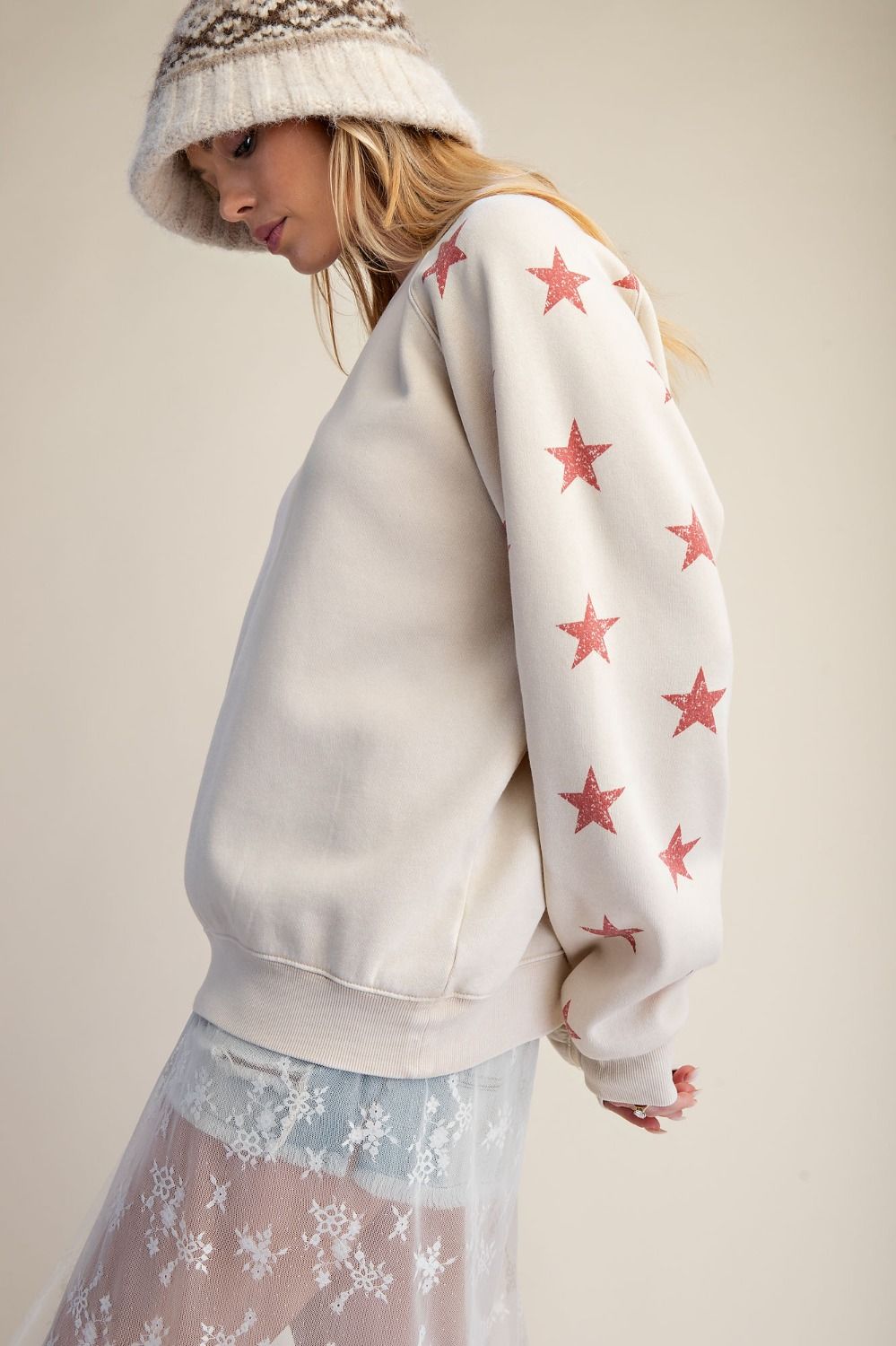 Woman wearing a white sweatshirt with red star patterns and a light skirt on a plain background