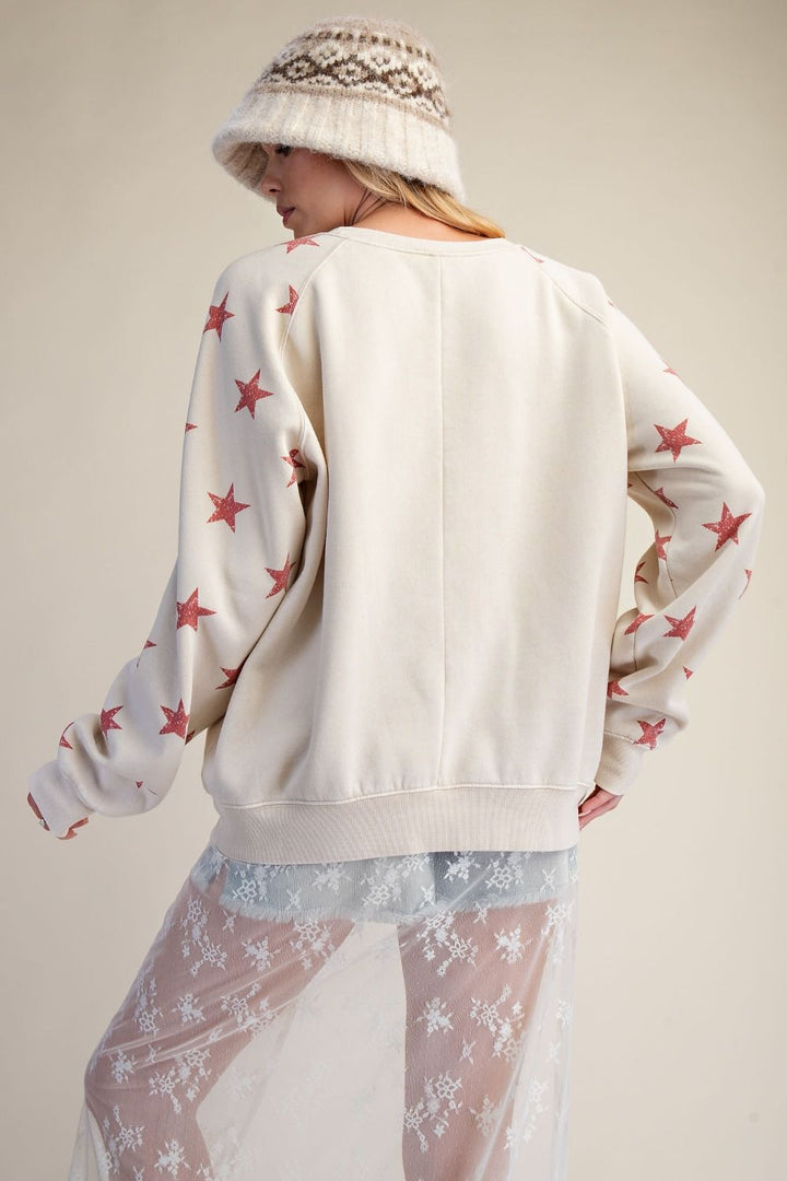 Person wearing a white sweater with red star patterns and a patterned hat on a beige background