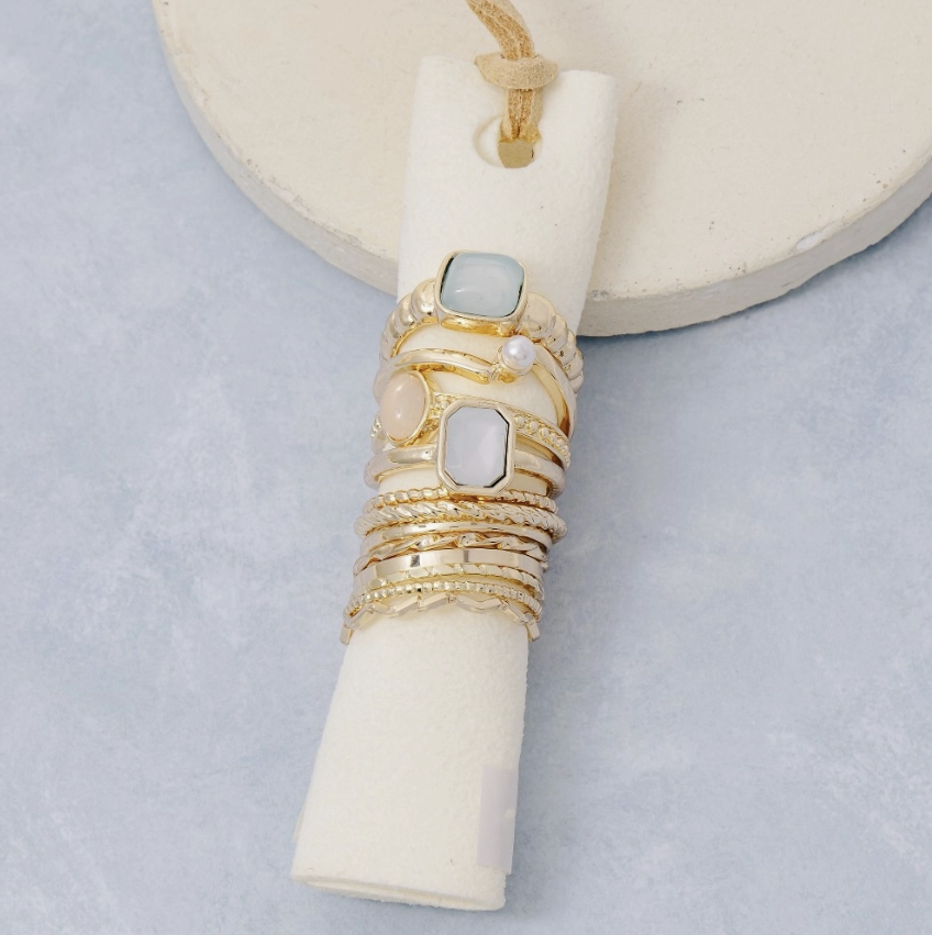 Ring stack with gold rings and blue and pink stones on plain background