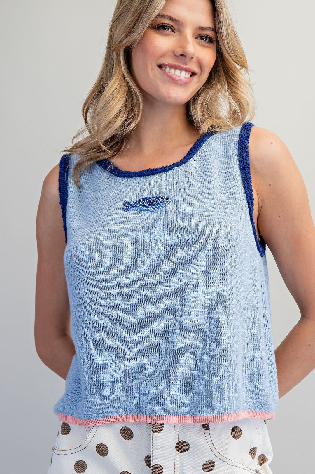 Woman wearing blue tank top with beaded fish detail on plain background