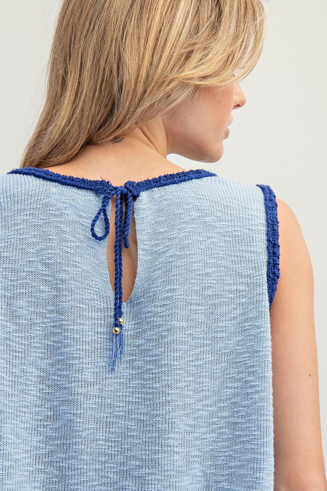 Back of woman wearing blue knit tank on plain background