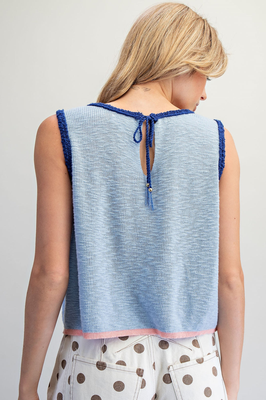 Back of woman wearing blue knit tank on plain background