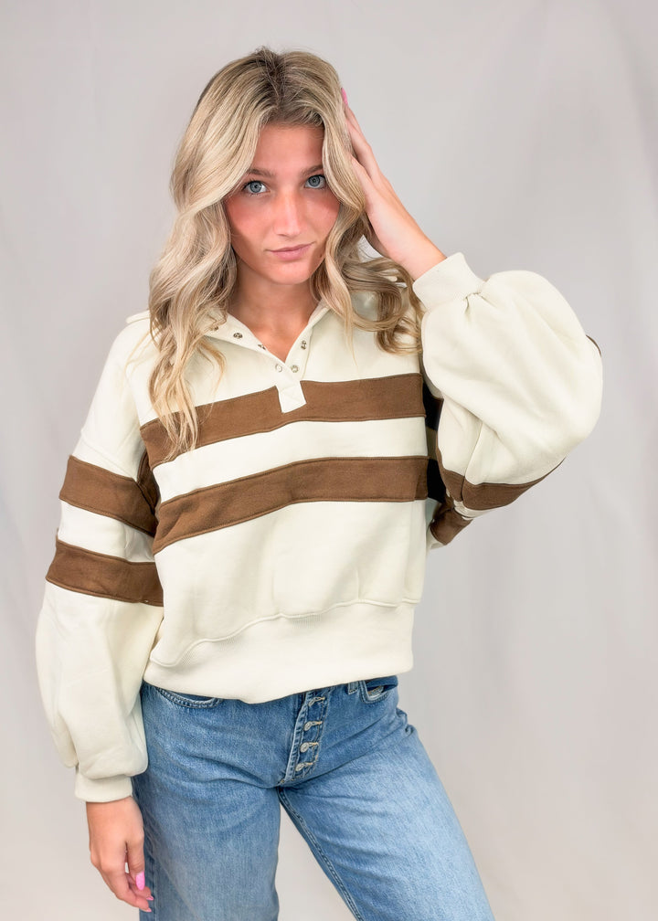 Woman wearing beige sweatshirt with brown stripes and jeans on plain background