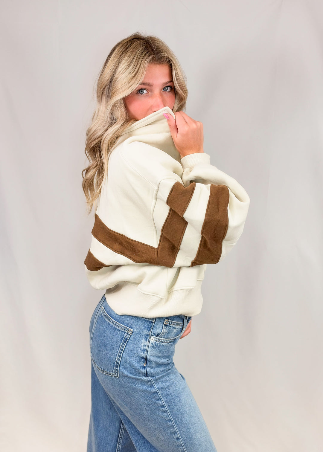 Woman wearing cream sweatshirt with brown stripes and jeans on plain background