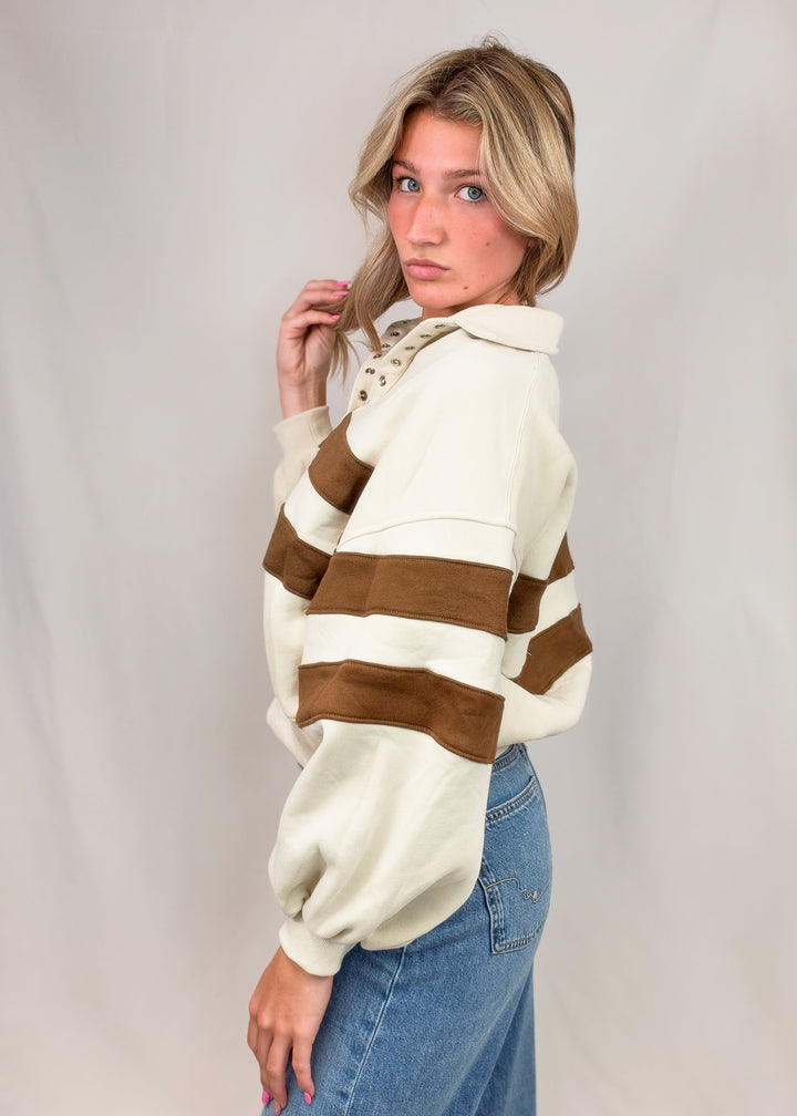 Woman wearing cream sweatshirt with brown stripes and jeans on plain background
