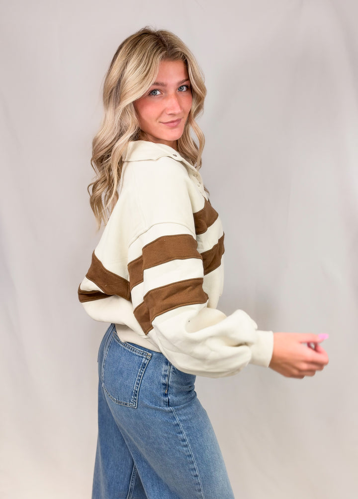 Woman wearing cream sweatshirt with brown stripes and jeans on plain background