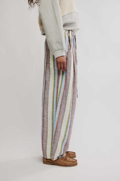 Person wearing a light gray sweater and colorful striped pants on a white background
