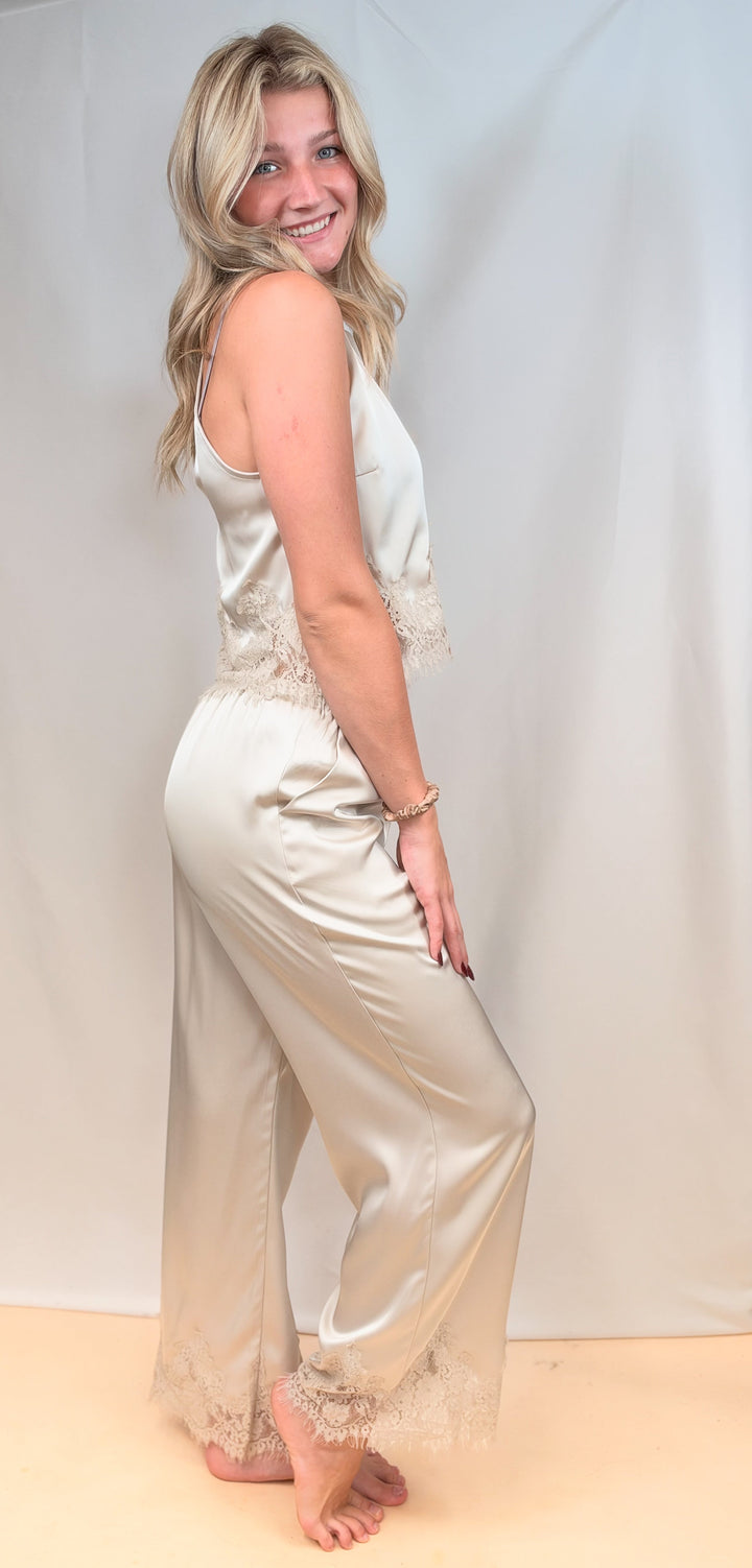Woman shown from side view wearing beige satin matching set with lace detail on plain background