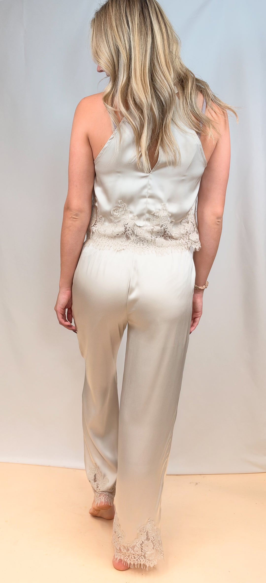 Woman shown from back view wearing beige satin matching set with lace detail on plain background