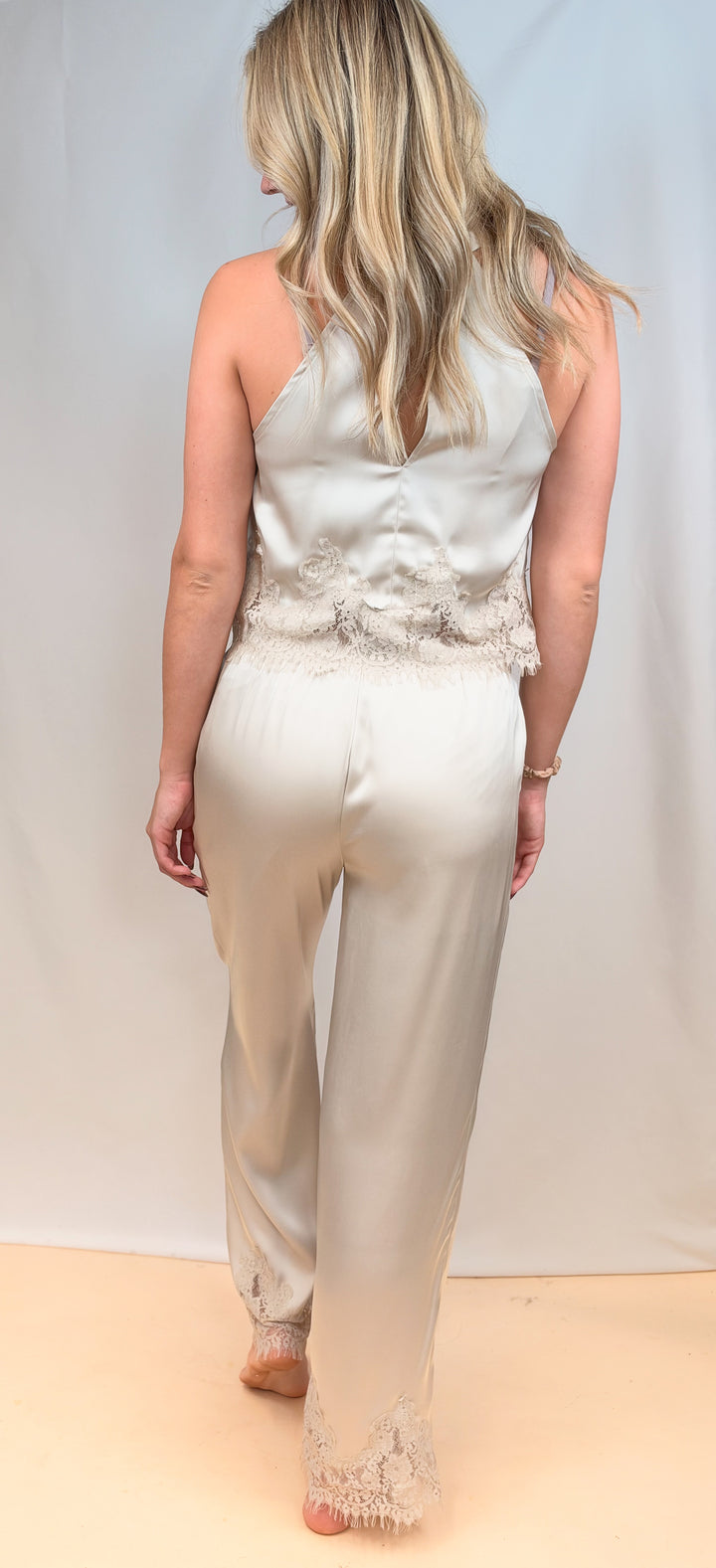Woman shown from back view wearing beige satin matching set with lace detail on plain background
