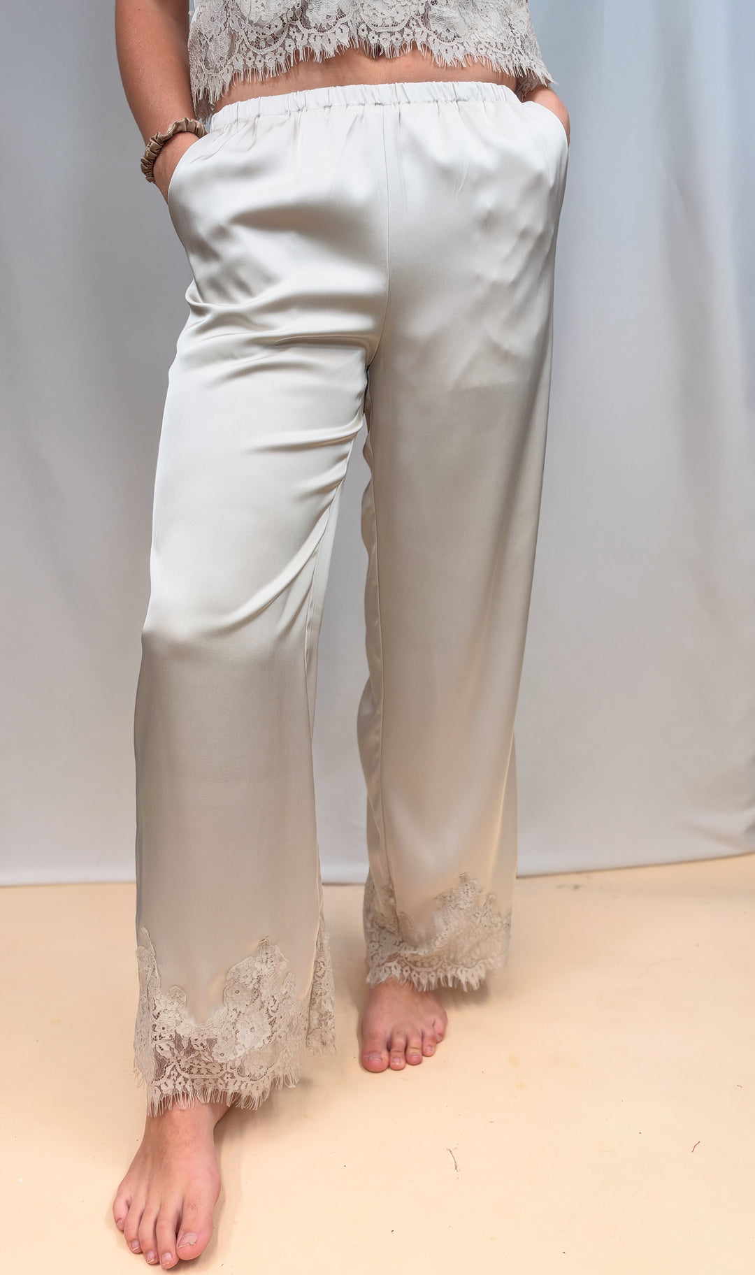 Woman shown from waist down wearing matching beige satin set with lace detail on plain background