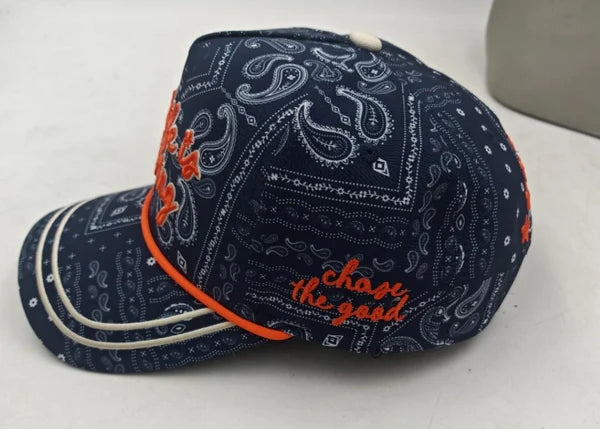 Navy blue cap with orange and white bandana pattern and 'Chase the Good' text on a light gray background