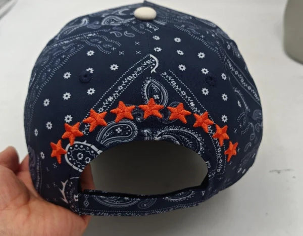 Navy blue cap with white patterns and orange stars held by a hand on a light background