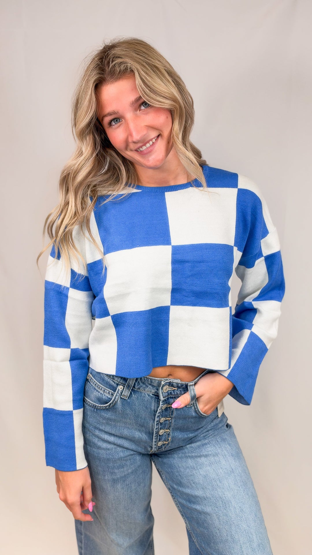 Woman wearing blue and white checkered crop sweater with jeans on plain background