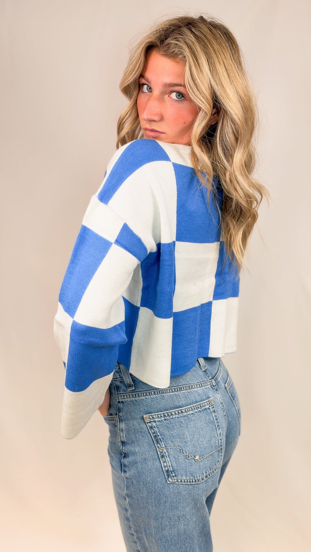 Woman wearing blue and white checker crop sweater with jeans on plain background