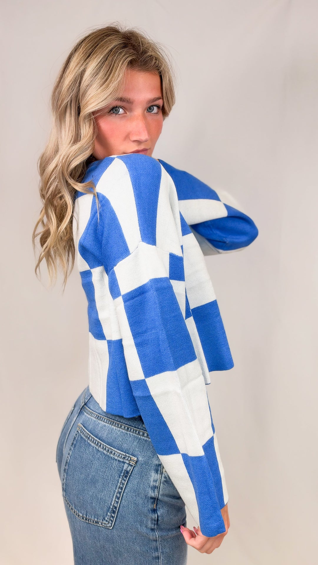 Woman wearing blue and white checker crop sweater with jeans on plain background