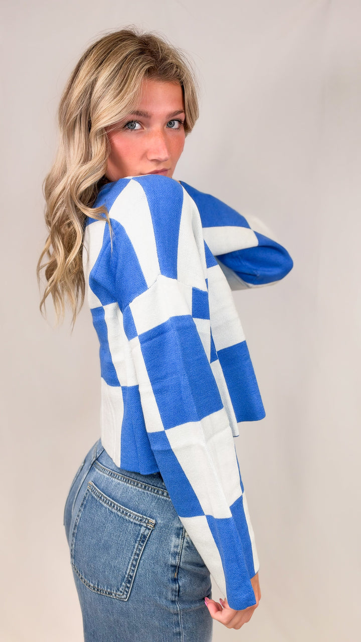 Woman wearing blue and white checker crop sweater with jeans on plain background