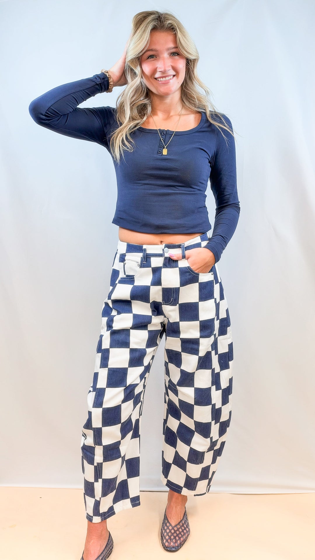 Woman wearing blue and white checkered barrel pants with navy top on plain background