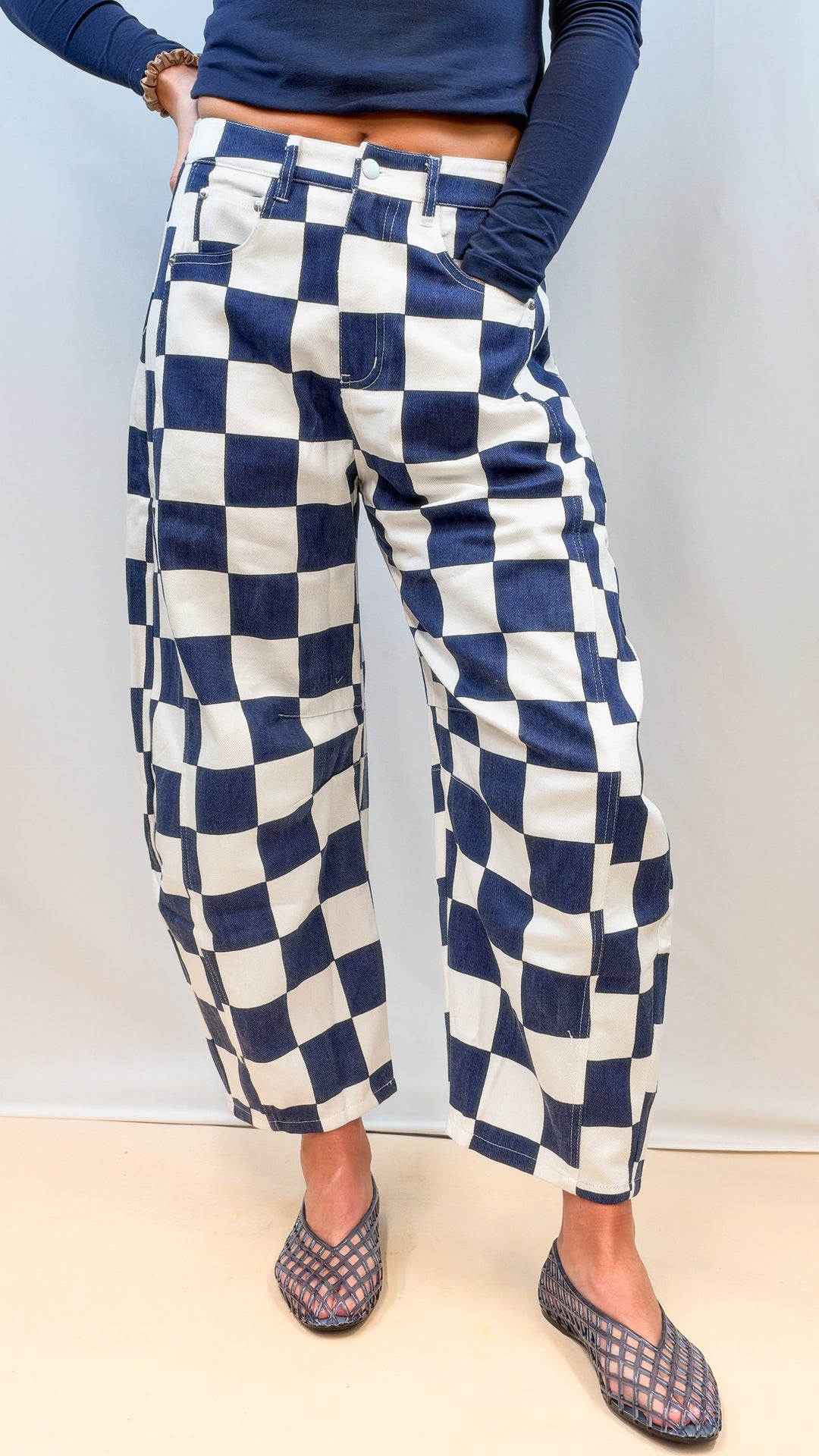Woman wearing navy and white checkered barrel pants with navy top on plain background