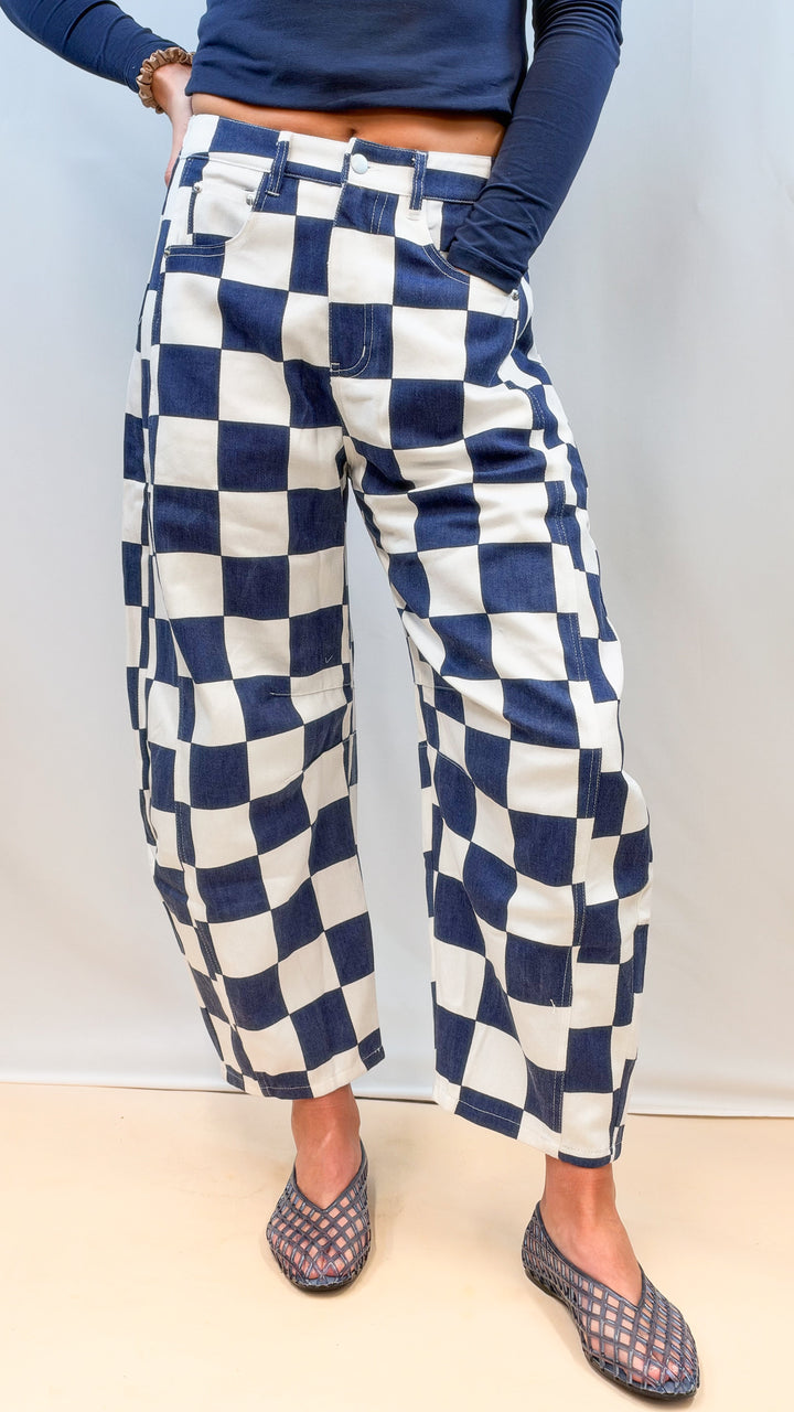 Woman wearing navy and white checkered barrel pants with navy top on plain background
