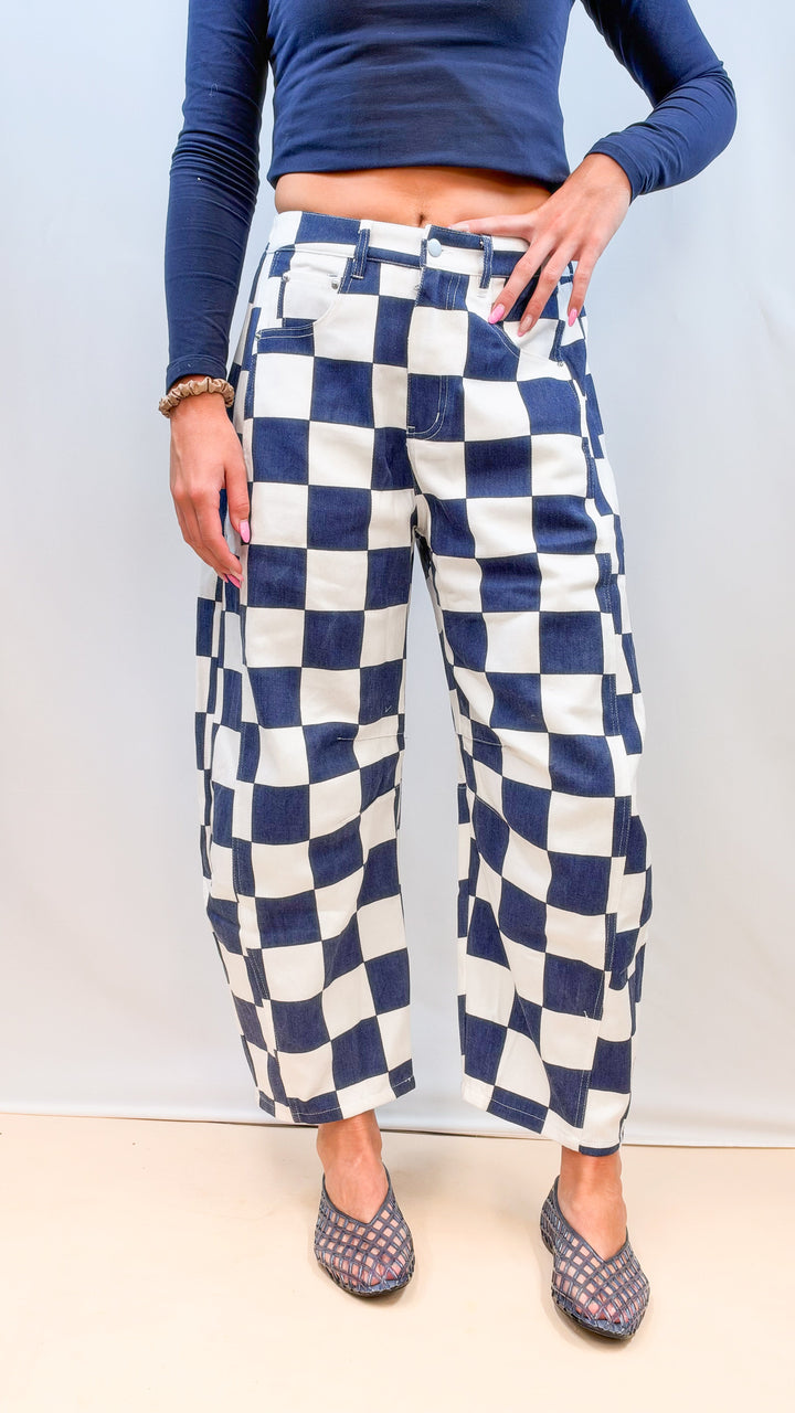 Woman wearing navy and white checkered barrel pants with navy top on plain background