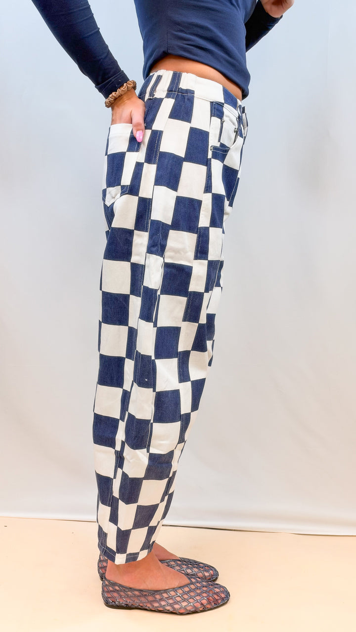 Woman wearing navy and white checkered barrel pants shown from side on plain background