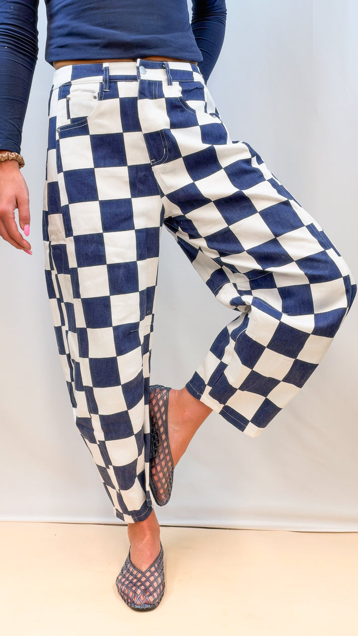 Woman wearing navy and white checkered barrel pants with navy top on plain background