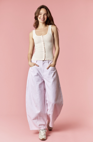 Woman wearing a cream sleeveless top and pink striped pants on a pink background